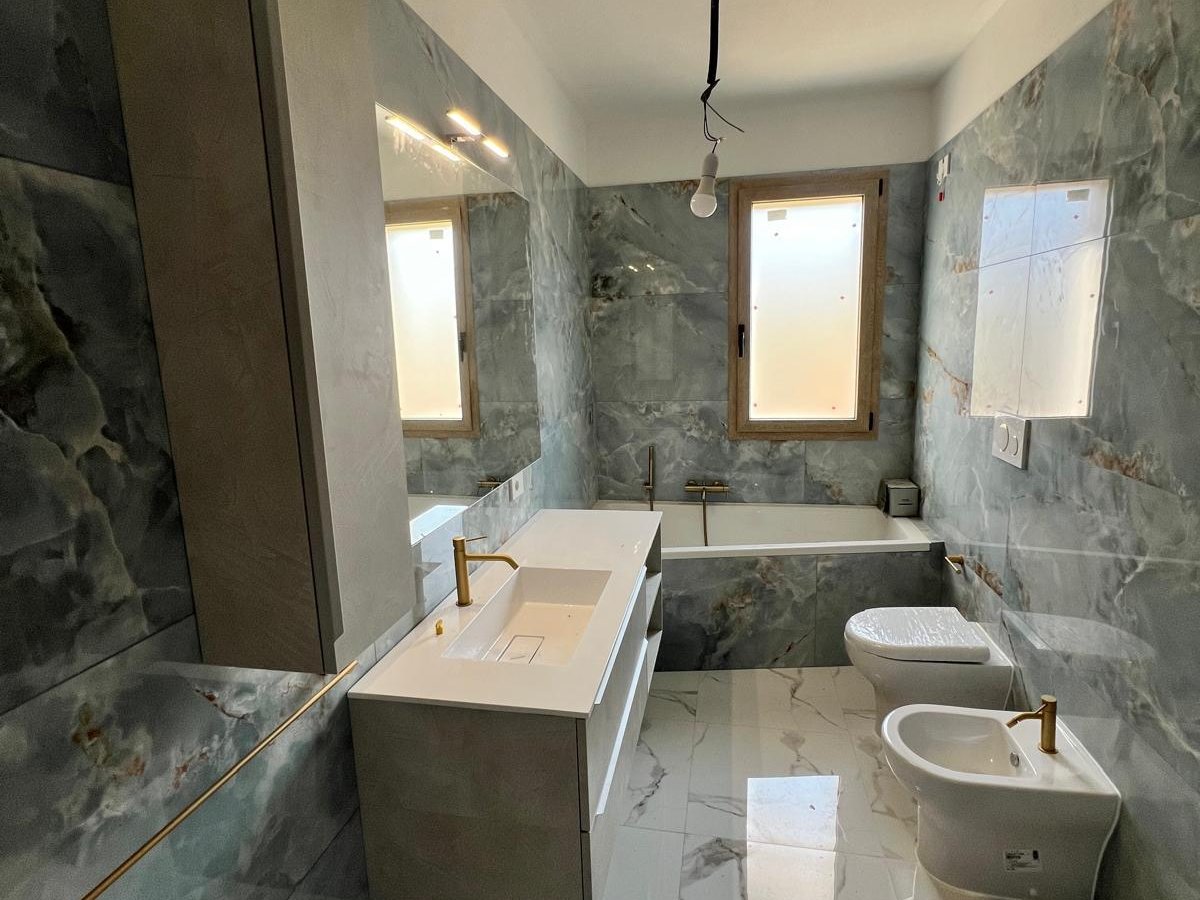 Bagno completato con rivestimento in lastre di onice, vasca incassata e pavimento chiaro